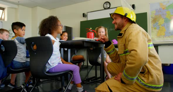 Young handsome Caucasian male firefighter teaching schoolgirl about fire safety in classroom 4k