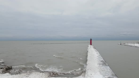 Looking out onto Lake Michigan with pier leading to lighthouse in winter. Waves creating ice on pier