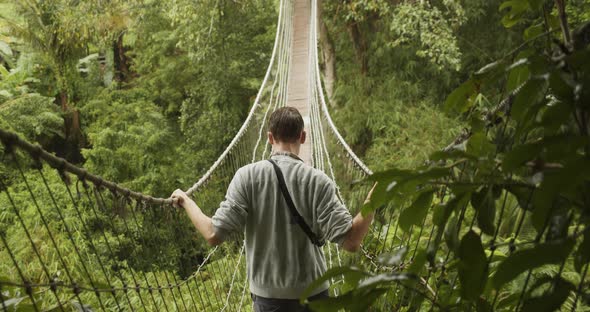 Back Close Up View of a Man Making His Way Across an Unstable Rope Jungle Bridge in the Rain Young