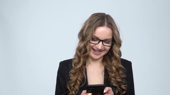 Smiling Woman Texting on Her Phone on Gray Background in Studio, Slow Motion