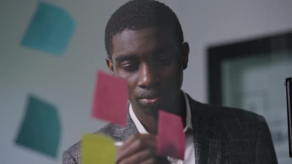 Closeup Portrait of Focused African American Young Man Writing with Pen on Sticky Notes Standing