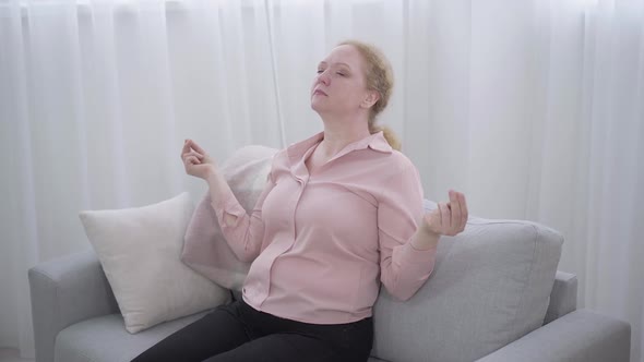 Confident Caucasian Woman Calming Down Using Yoga. Portrait of Calm Senior Lady Sitting on Couch