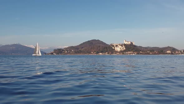 Low-angle sea-level view of small boat sailing on Maggiore lake with snowy mountains in background.