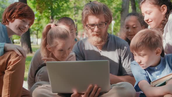 Male Teacher Showing Something on Laptop to Kids in Park