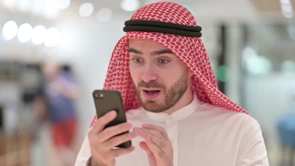 Portrait of Excited Arab Businessman Celebrating Success on Smartphone