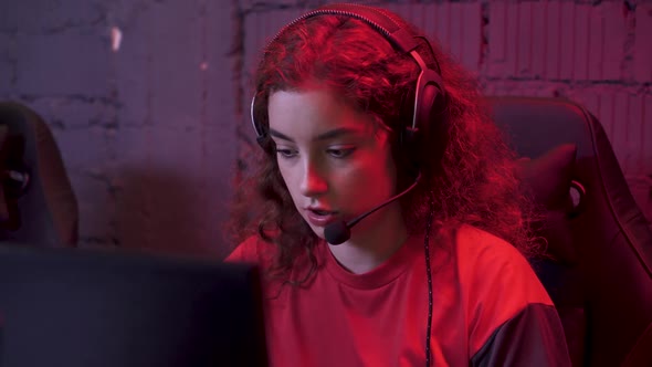 Young Girl Gamer in Headphones Plays a Video Game and Communicating with a Team of Players Cyber