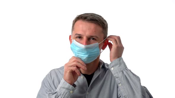 A Young Man on a White Isolated Background Puts on a Surgical Mask To Protect From Allergens and