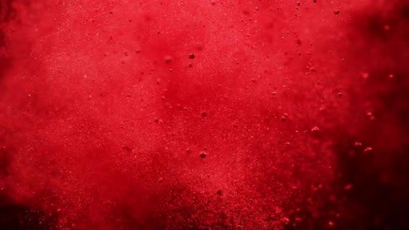 Red powder/particles fly after being exploded against black background. Slow Motion.