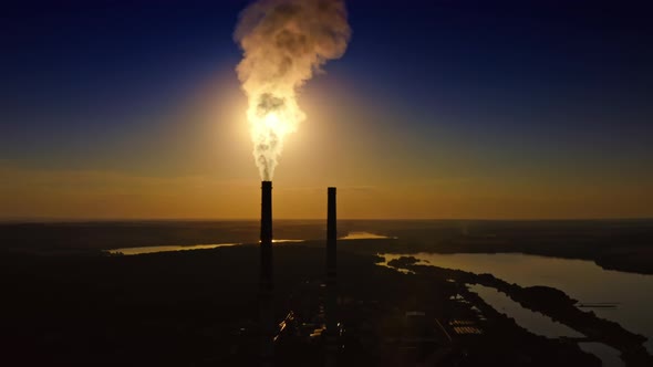 High chimneys of industrial plants smoke against background of nature and river. 