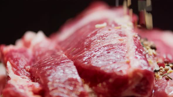 Large Cut Piece of Raw Fresh Beef Meat on a Black Blurry Background is Sprinkled with Spices