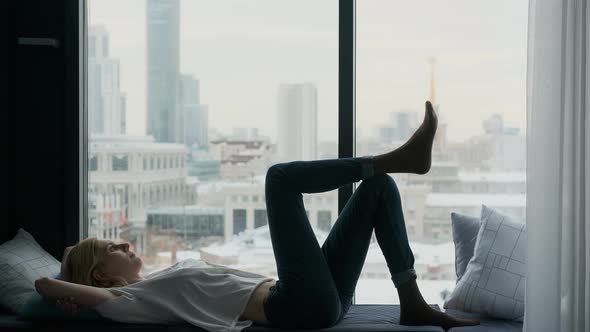 woman relaxed lying on the windowsill by the window overlooking the city