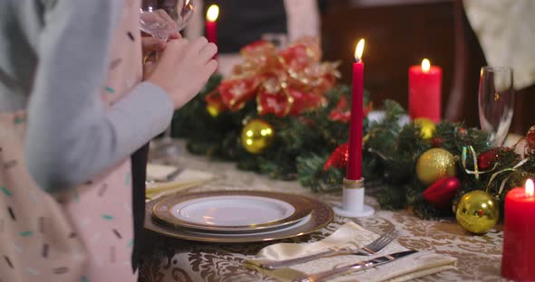 Unrecognizable Caucasian Boy Passing Camera Putting Drinking Glass on Decorated Christmas Table and