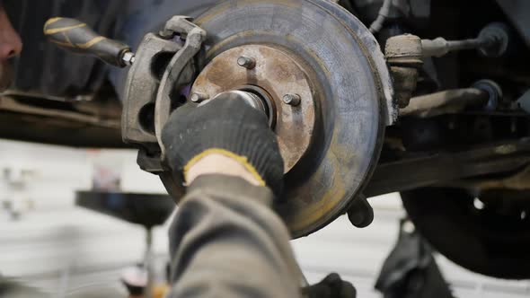 Male Car Mechanic with a Wrench Tightens the Nut on the Front Hub of the Car