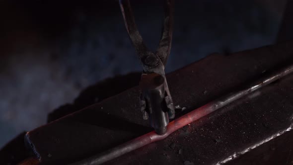 Anonymous young blacksmith using hammer while forging iron on anvil