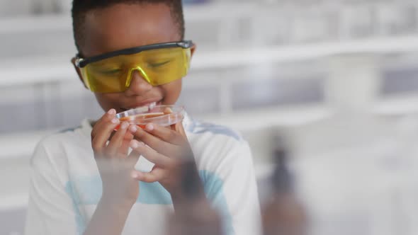 Video of happy african american boy wearing glasses and holding reagent during chemistry lesson