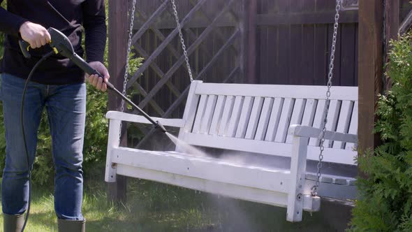 Caucasian Man Washes Dirt Off a Wooden Bench Swing Using a High Pressure Washer