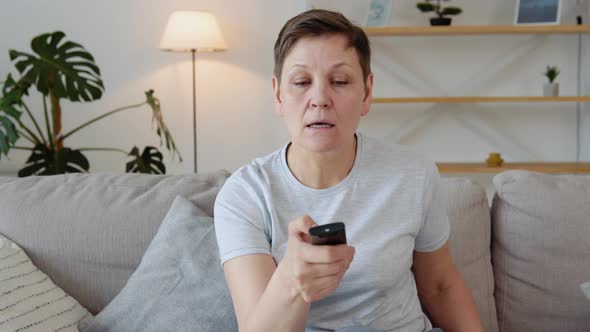 Senior Lady Watching Tv in Living Room Sitting on Sofa Holding Remote Control Changing Tv Channels