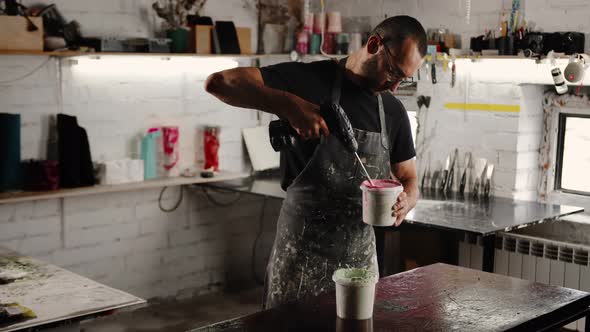 A male handyman mixes paint in a can in a workshop. A sculptor mixes resin with paint to a vase.