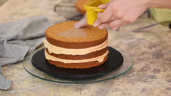 Unrecognizable female confectioner hand soaks sponge cake with sweet caramel syrup