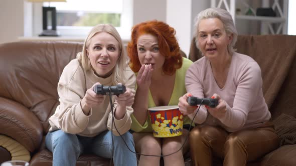 Adult Female Gamers Competing in Video Game with Friend Supporting Eating Popcorn