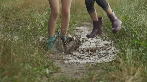 Legs of Two Children Girls in Boots Jumping in Rainy Little Puddle