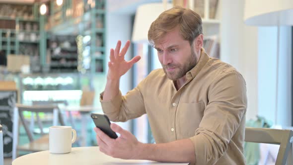 Disappointed Man Reacting To Loss on Cellphone in Cafe