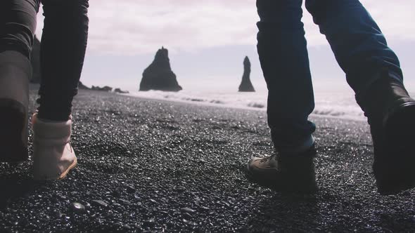 Close Up Shot of Young Couple Holding Hands Walking Down Black Sand Beach in Iceland Slow Motion