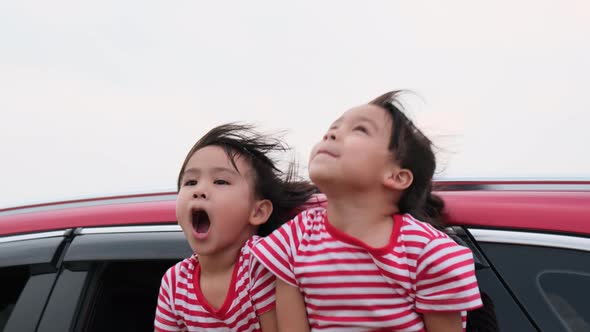 Cute Asian siblings girls smiling and having fun traveling by car and looking out of the car window.