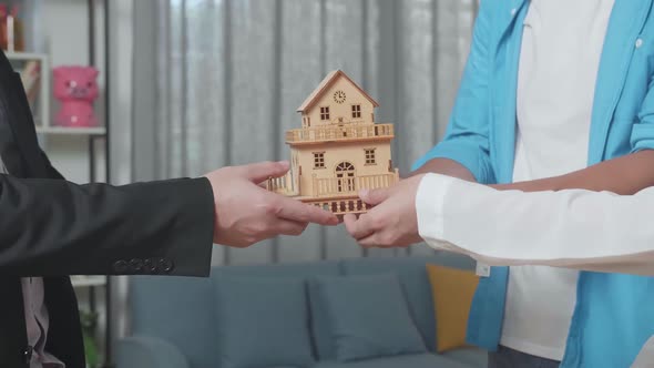 Close Up Of Couple'S Hands Receiving The House Model From A Real Estate Agent In The House For Sale