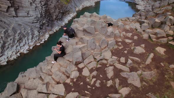 Tourists by the Large Rock on a Cliff with River in the Middle - Iceland