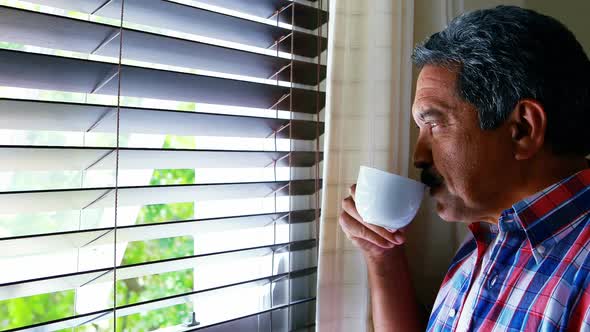 Senior man looking through window while having coffee 4k