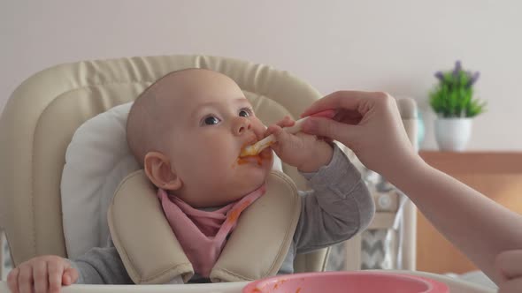 A newborn baby with a spoon tries to eat on its own. Feeding a newborn with pumpkin puree