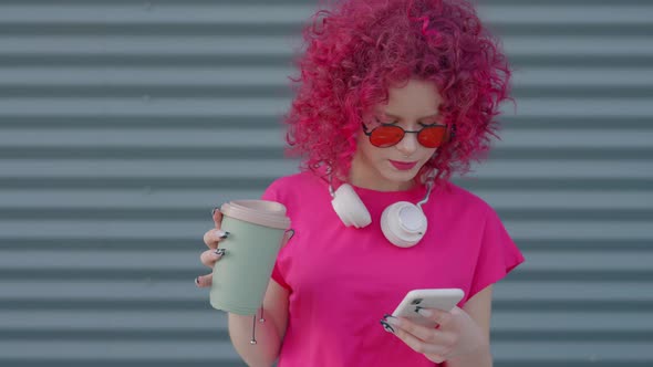 A Pink Curly Teenager is Using a Smartphone Outdoors