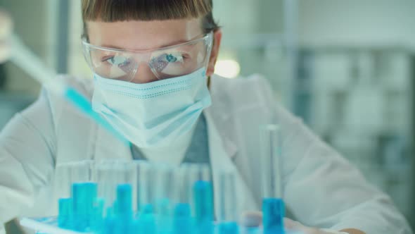 Woman in Mask and Gloves Pouring Blue Chemical in Test Tubes
