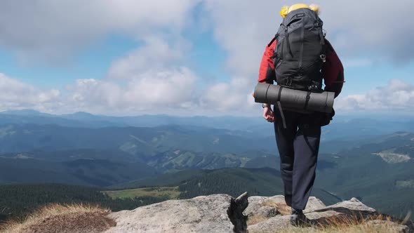 Tourist with Backpack on the Top of Mountain Near the Cliff Raises Hands To Side