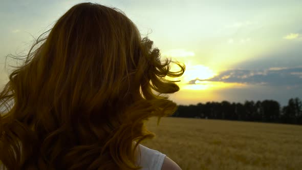 Wind stirring red hair of romantic girl at sunset