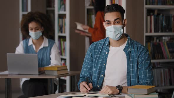 Students in Library Young Indian Guy in Protective Mask Sits at Desk Doing Homework Preparing for