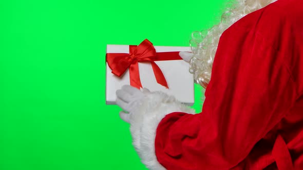 View From Behind Santa Claus with Beard in White Gloves and a Red Suit Twirls a Gift Box in His