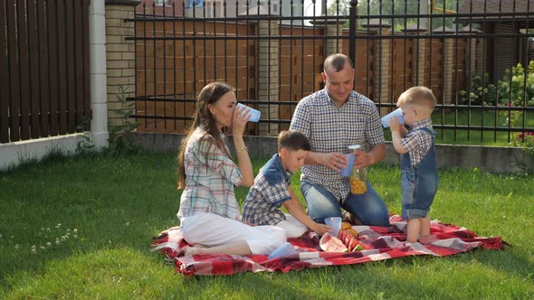 Happy Family Sits on Blanket and Father Pours Orange Juice