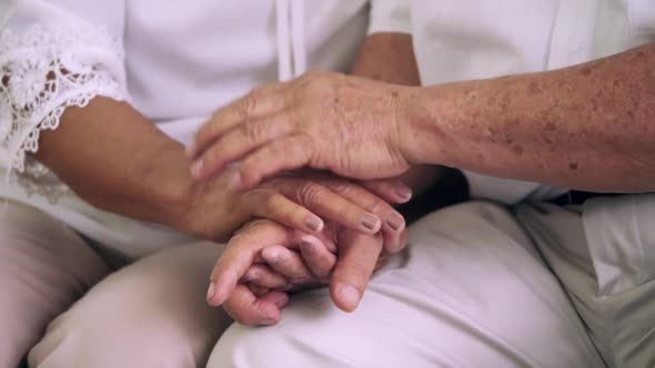 Close up of elderly couple holding hands together at home.