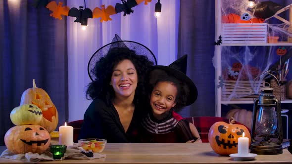 Mom and Daughter African American in Festive Costume and Witch Hat Have Fun and Hug Joyfully