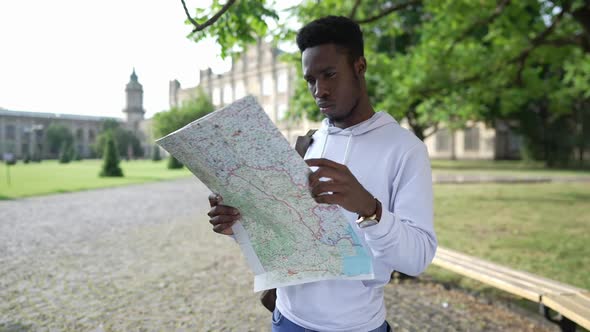 Portrait of Concentrated African American Young Man with Paper Map Standing at University Campus