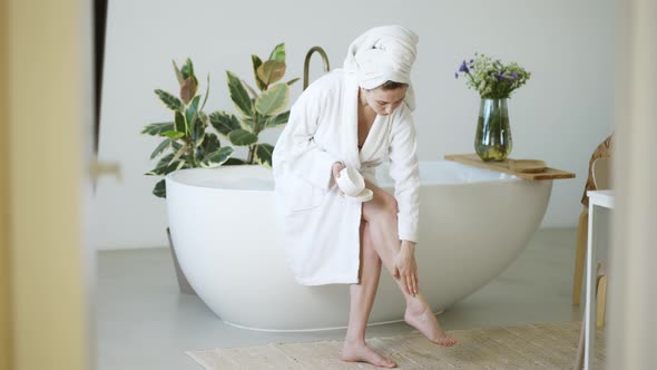 Beautiful Young Woman Applying Cream on Her Legs in Bathroom