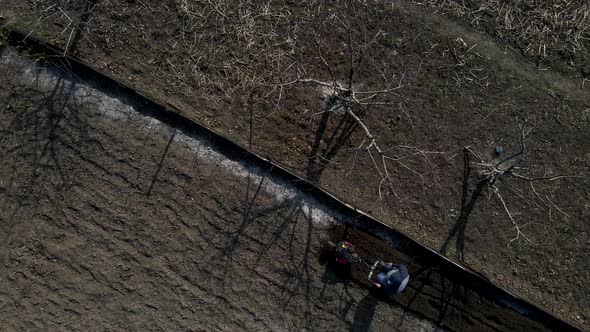 Aerial Drone View Man Farmer Working in the Garden Plows with Garden Tiller