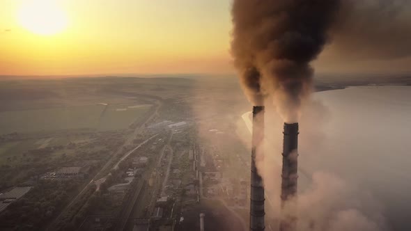 Aerial view of coal power plant high pipes with black smoke moving up polluting atmosphere at sunset