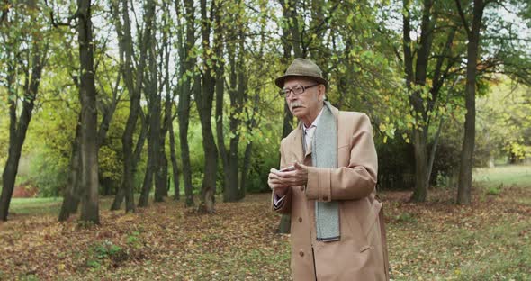 Elegant Senior Man Looks Around and Notes Something During a Walk in Green Park