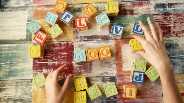 Top View of the Desktop. Women's Hands Add the Word "BOOK" From Wooden Cubes