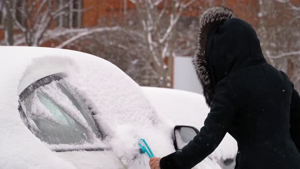 Woman Cleans the Car of Snow in Winter in Cold Weather