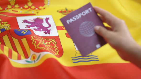 Female Hand Putting International Red Passport on Spanish Flag, Citizenship