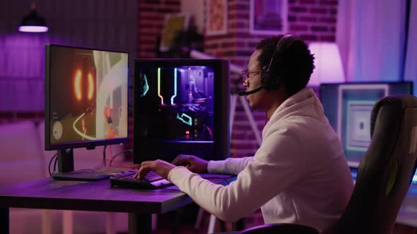 African American Gamer Relaxing Playing Online Action Game Using Pc Gaming Setup and Talking to Team